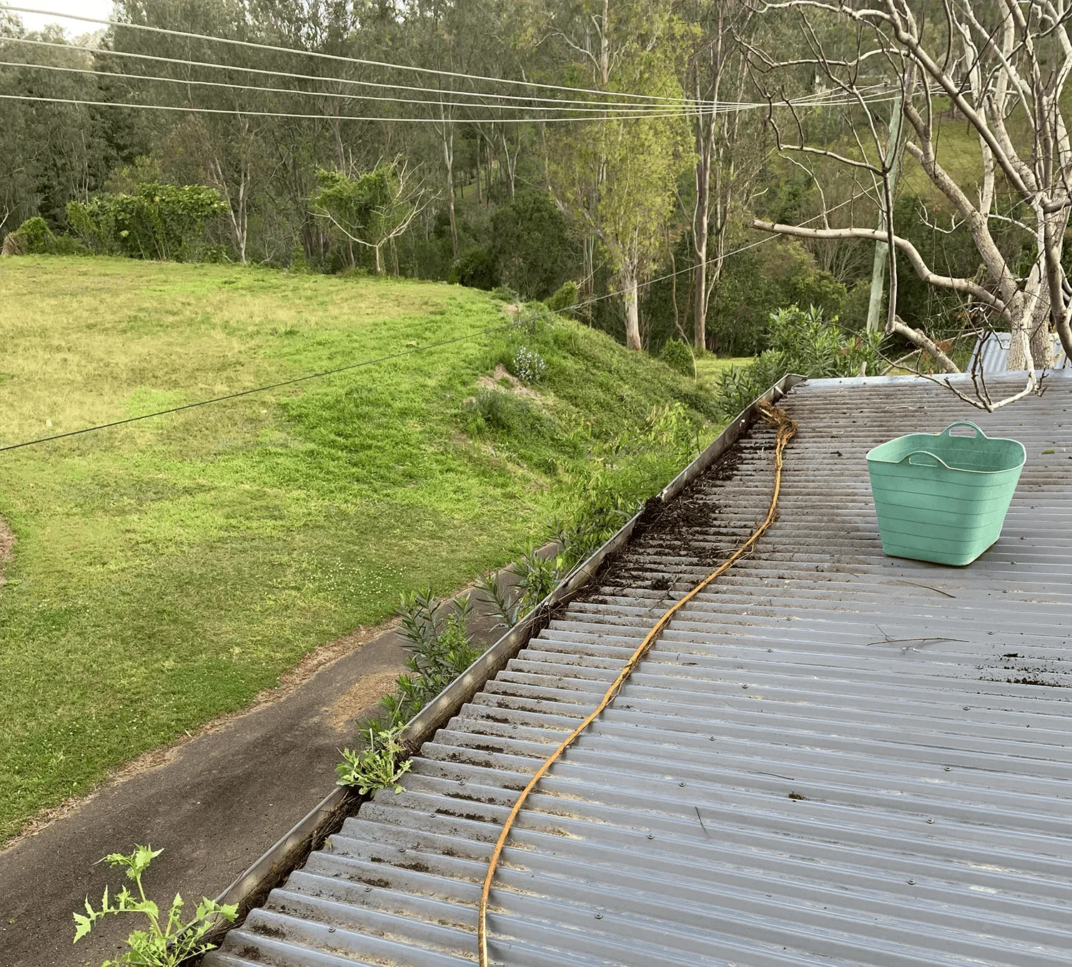 Dirty gutters in the process of being cleaned with a green bucket of water.