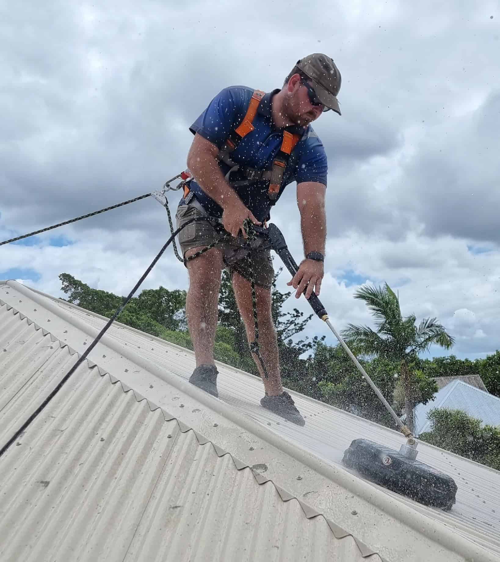 A handyman pressure cleaning a beige roof