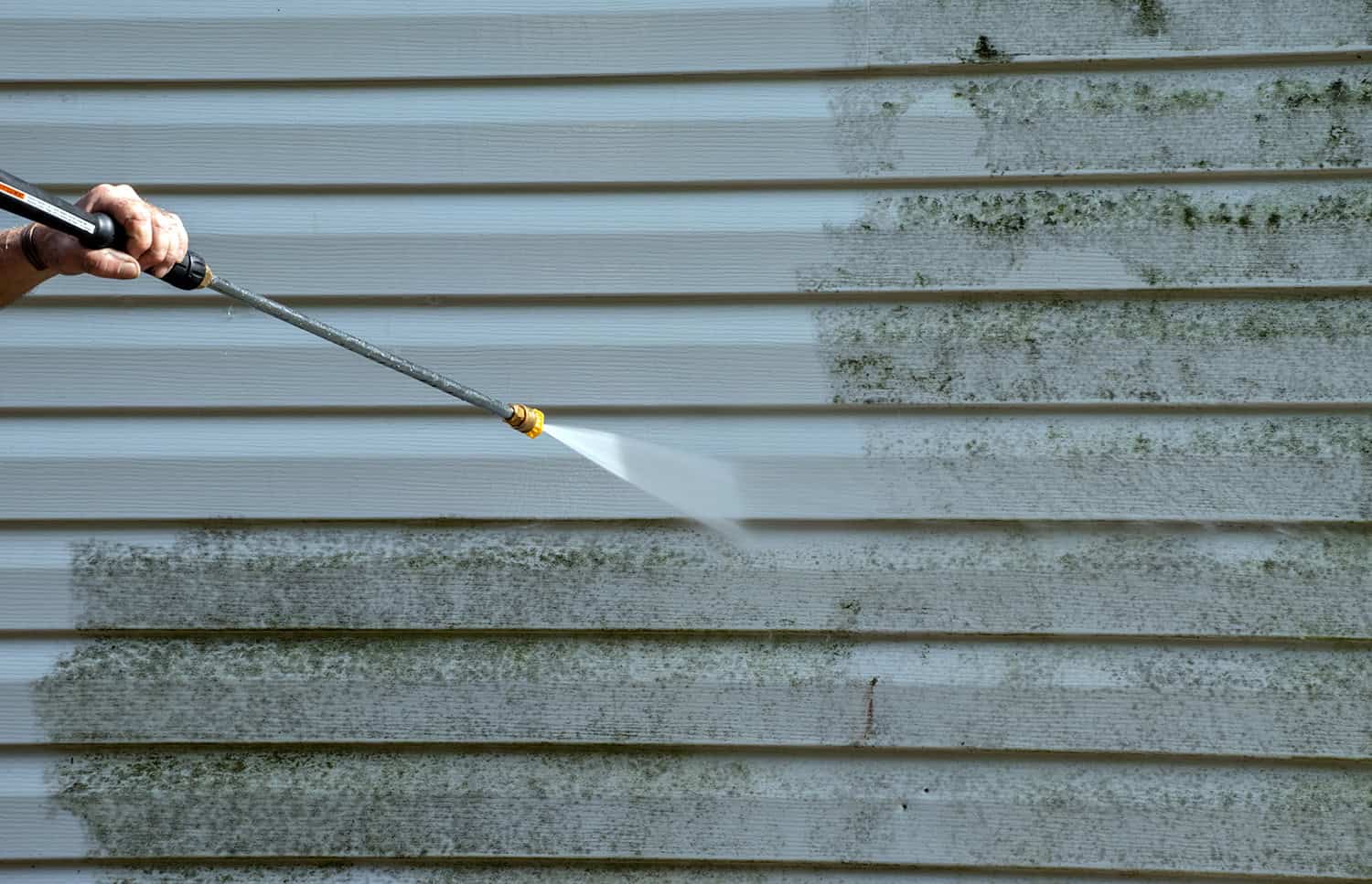 A handyman pressure cleaning the mould off an exterior wall