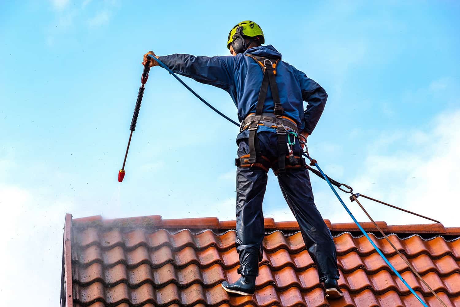 A worker on a terracotta roof pressure cleaning